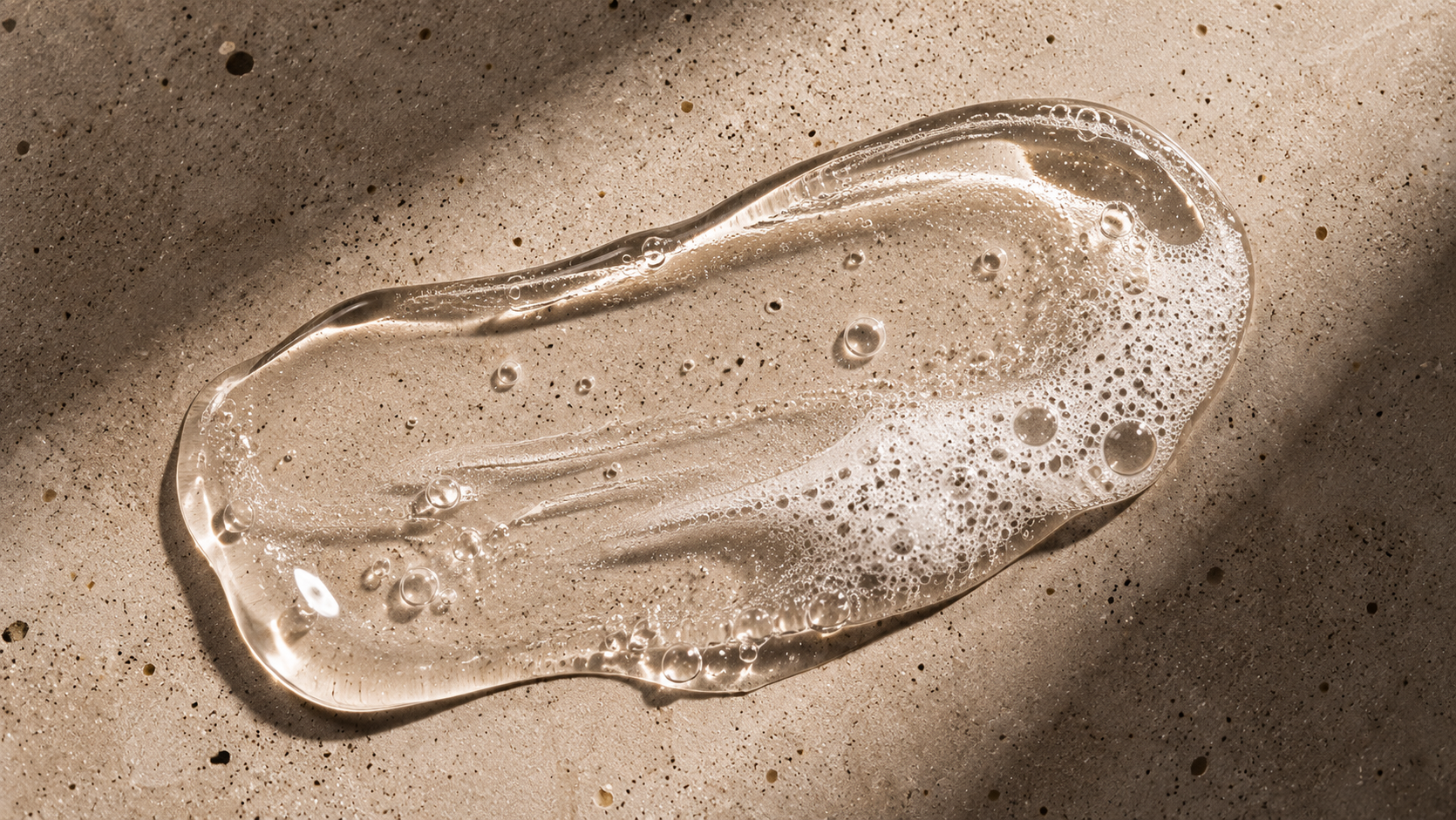 A smear of The Bald Guy scalp cleanser gel texture with light foam, shown on a stone surface